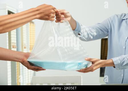 Unrecognizable delivery man passing container with business lunch to client while standing at spacious office lobby, close-up shot Stock Photo