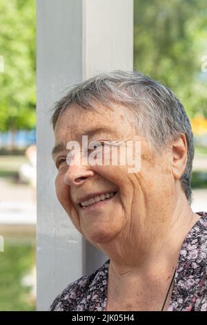 cheerful senior woman chatting with friends, laughing outdoors, looking side. beautiful aged woman enjoying on walk outdoors in summer, National Grand Stock Photo