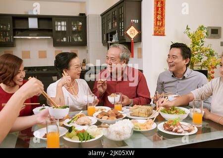 Family enjoying talk and good food at Chinese New Year celebration. Scrolls wishing luck and wealth in the background Stock Photo