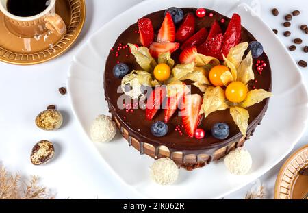 Chocolate cake with strawberries, bog whortleberry, physalis and Easter quai eggs on white plate. cake three chocolate with cup of fragrant coffee for Stock Photo