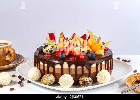 Chocolate cake with strawberries, bog whortleberry, physalis and Easter quai eggs on gray background. cake three chocolate on white plate with cup of Stock Photo