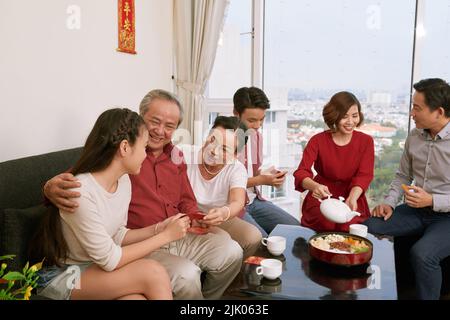Family drinking tea and giving traditional lucky money envelopes to children at Tet celebration Stock Photo