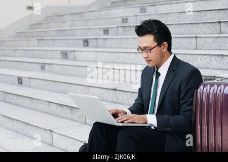 Young businessman sitting outdoors and working on laptop Stock Photo