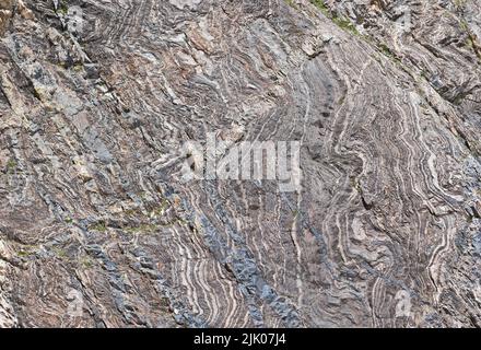 Detail of grey, deformed and curved layers in rock, caused by geological forces, natural background Stock Photo