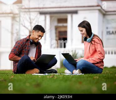 We always help each other out. two students using their laptops while sitting outside on campus. Stock Photo