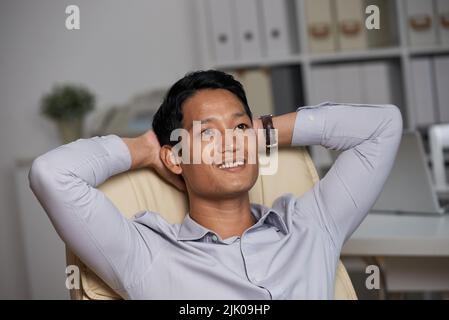 Portrait of dreamy Vietnamese businessman sitting in chair Stock Photo