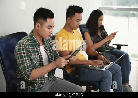 Vietnamese young people busy with work on various devices Stock Photo