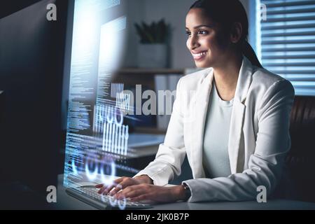 Were getting closer to success. an attractive young businesswoman sitting alone in her office at night and using her computer. Stock Photo