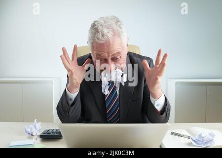 Furious elderly businessman wearing classical suit sitting at office desk and eating contract after unsuccessful completion of negotiations, portrait shot Stock Photo