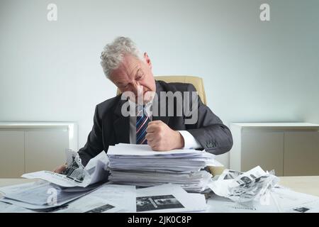 Waist-up portrait of furious aged entrepreneur wearing classical suit crumpling documents while relieving stress at modern office Stock Photo