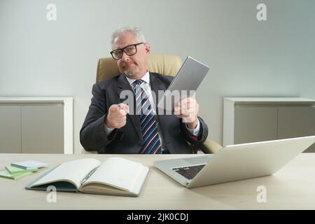Waist-up portrait of confident senior white collar worker wearing eyeglasses pointing at camera with index finger while holding digital tablet in hand Stock Photo