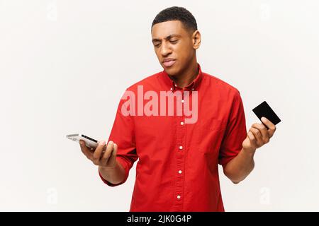 Latin man worrying about money. Confused man holding credit card and smartphone with disappointed face, shrugging, bankruptcy concept Stock Photo