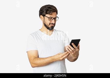 Portrait of a young man, cheerful, wearing a T-shirt, standing, isolated on a white background, using a cell phone. Stock Photo