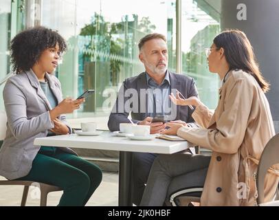 We need to begin work on that immediately. a group of colleagues brainstorming ideas at a coffee shop while using their smartphones. Stock Photo