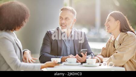 Our business is about to soar. a group of colleagues brainstorming ideas at a coffee shop while using their smartphones. Stock Photo