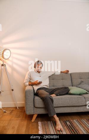 Ginger bristle man using mobile phone while resting on couch at home Stock Photo