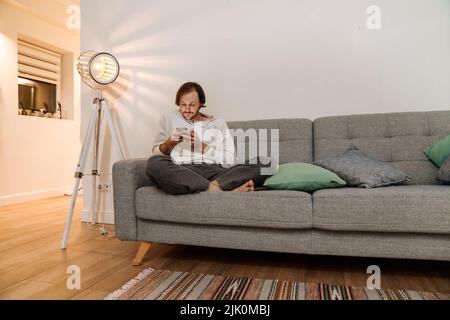 Ginger bristle man using mobile phone while resting on couch at home Stock Photo