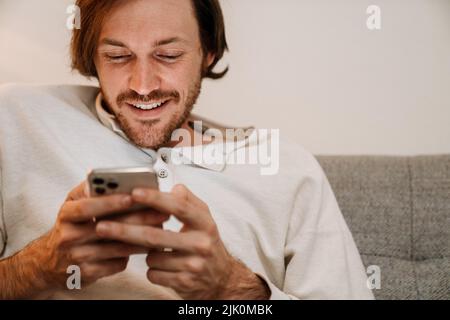 Ginger bristle man using mobile phone while resting on couch at home Stock Photo
