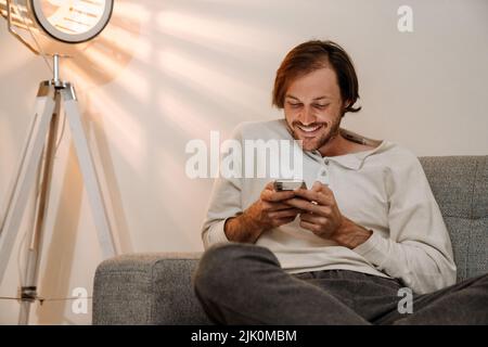 Ginger bristle man using mobile phone while resting on couch at home Stock Photo