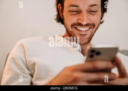 Ginger bristle man using mobile phone while resting on couch at home Stock Photo