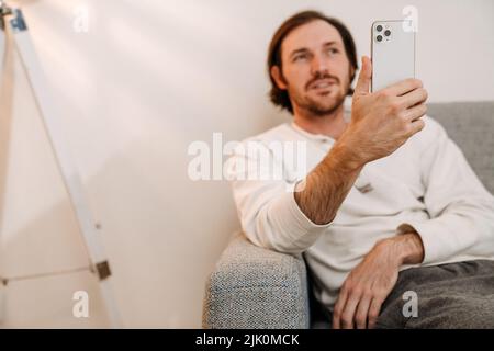 Ginger bristle man using mobile phone while resting on couch at home Stock Photo