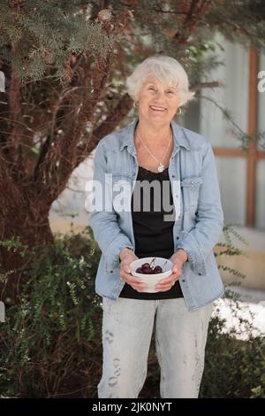 Elderly woman holding bowl of ripe cherries Stock Photo