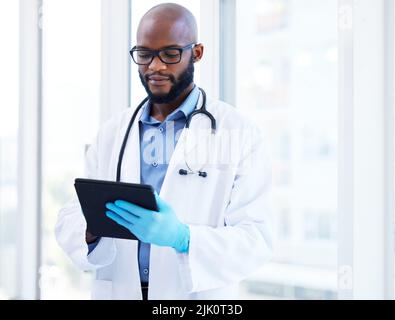 Getting ready for a busy day at the clinic. a handsome young doctor standing alone in his clinic and using a digital tablet. Stock Photo