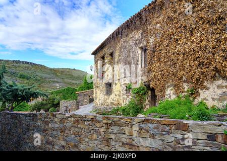 Old facade of ancient house covered with ivy and blue sky with clouds. Patones de Arriba Madrid. Spain. Stock Photo