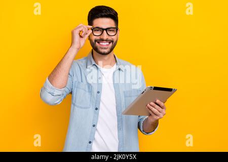 Portrait of young man showing new glasses using tablet distant work isolated on yellow color background Stock Photo