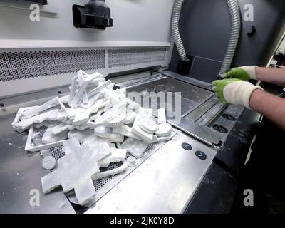 Man cleans details printed on industrial 3D printer from white plastic powder. Automated additive technologies. Person cleans vacuum cleaner plastic powder from models printed on 3D printer. Top view Stock Photo