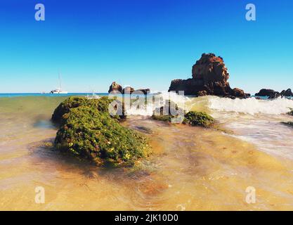 The sea waves crashing into algae-covered rock formations near Algarve beach in Portugal Stock Photo