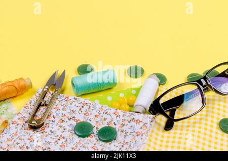 A set of sewing accessories for sewing, spools of thread, fabrics, scissors, thimble and glasses. Tailoring concept, patchwork and handwork.  Needlewo Stock Photo