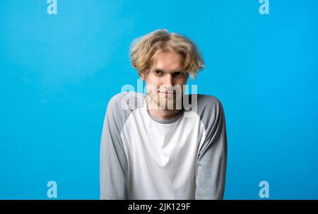 Portrait of young man in long sleeve t-shirt smiling looking at camera over blue background studio. Emotions. Stock Photo