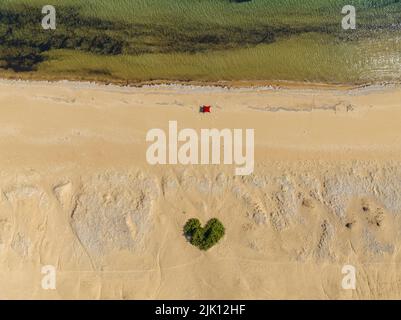 Aerial view of Paralia Issos beach in Corfu, Greece. Awning. Beach tent. Bathers. Bush in the shape of a heart in the middle of the sand. Love beach. Stock Photo