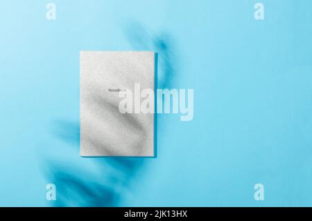 Blank notebook mockup with shadow of leaves on blue background. Elegant modern template for branding identity. Minimal nature background for summer co Stock Photo