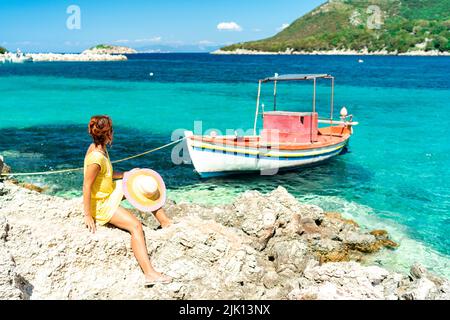 Woman sitting on rocks looking at boats in the turquoise sea, Porto Atheras, Kefalonia, Ionian Islands, Greek Islands, Greece, Europe Stock Photo