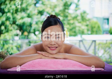 Happy relaxed Vietnamese young woman lying on massage bed in spa salon Stock Photo