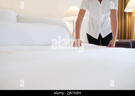 Maid putting clean white blanket on the bed Stock Photo