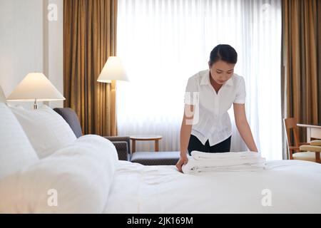 Maind putting fresh towels on the bed in hotel room Stock Photo