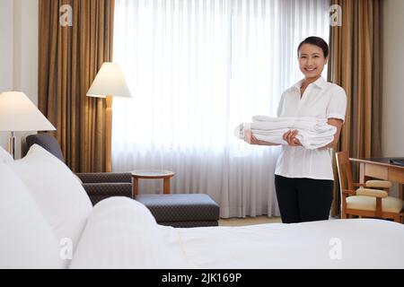 Happy young Asian chambermaid with a stack of fresh towels Stock Photo