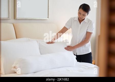 Chambermaid putting pillows on bed in hotel room Stock Photo