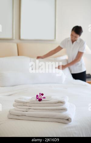 Maid making bed for the guests, focus on stack of towels Stock Photo