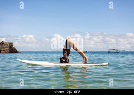 Woman stands upside down on a surfboard at Porto da Barra beach in Salvador, Bahia. Stock Photo