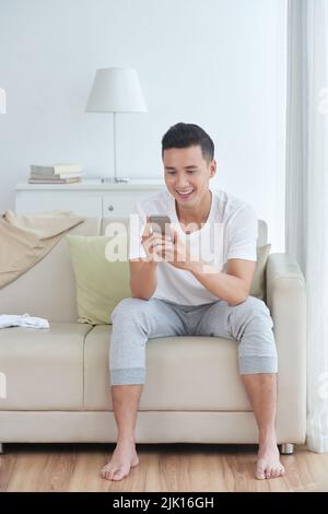 Cheerful young Asian man reading messages in his smartphone Stock Photo