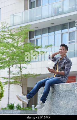 Happy young man with smartphone spending time outdoors Stock Photo