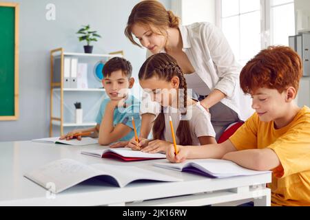 Caucasian girl and boys elementary school students perform task of female teacher sits in classroom Stock Photo