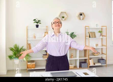 Happy senior business lady stretching her arms in office enjoying end of working day. Stock Photo