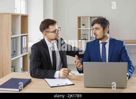 Two business people working in office, sitting at desk with laptop computer and talking Stock Photo