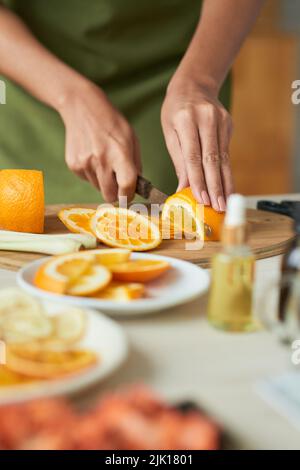 Hands of woman slicing ripe orange on cutting board Stock Photo