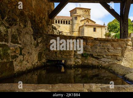 Fresh water fountain with stone church in medieval old town. Santillana del Mar, Santander. Stock Photo